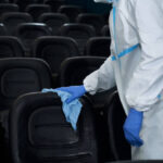 Close up worker in special clothes holding rag and wiping chairs in cinema. Concept of disinfection cinema hall.